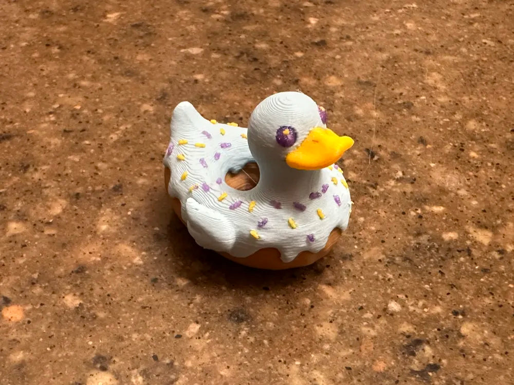 3D printed donut duck with white glaze, purple and yellow sprinkles, and yellow beak